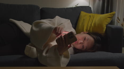 Woman-Spending-Evening-At-Home-Lying-On-Sofa-With-Mobile-Phone-Scrolling-Through-Internet-Or-Social-Media-9